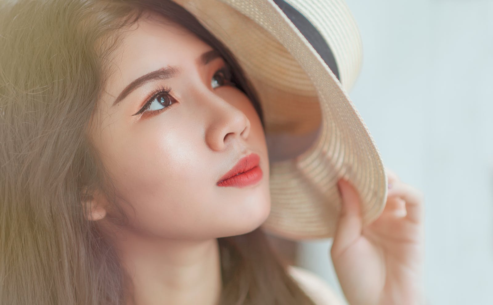 Close-up of a young woman with eye makeup holding a stylish hat.
