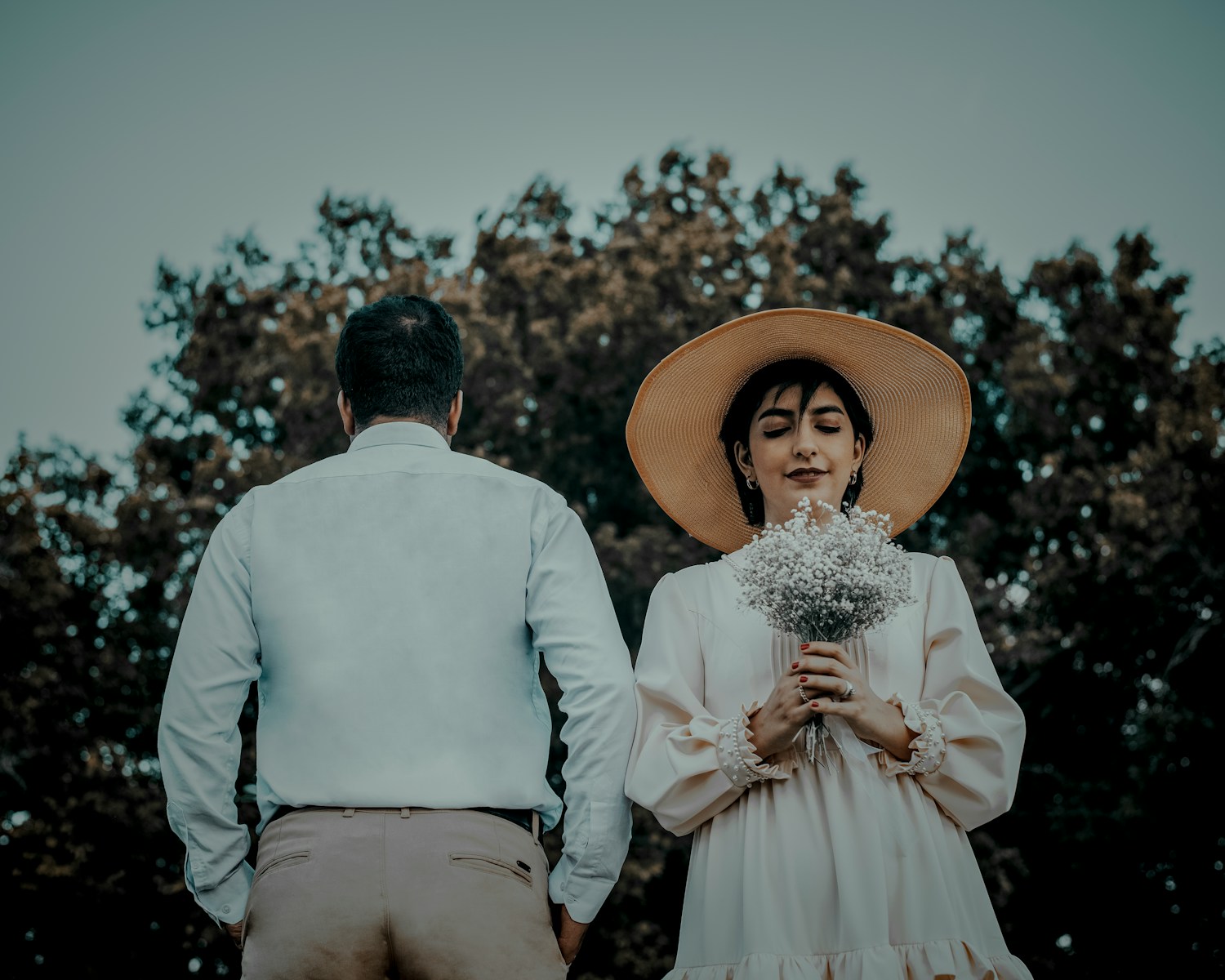 man in white dress shirt and brown hat holding white bouquet of flowers