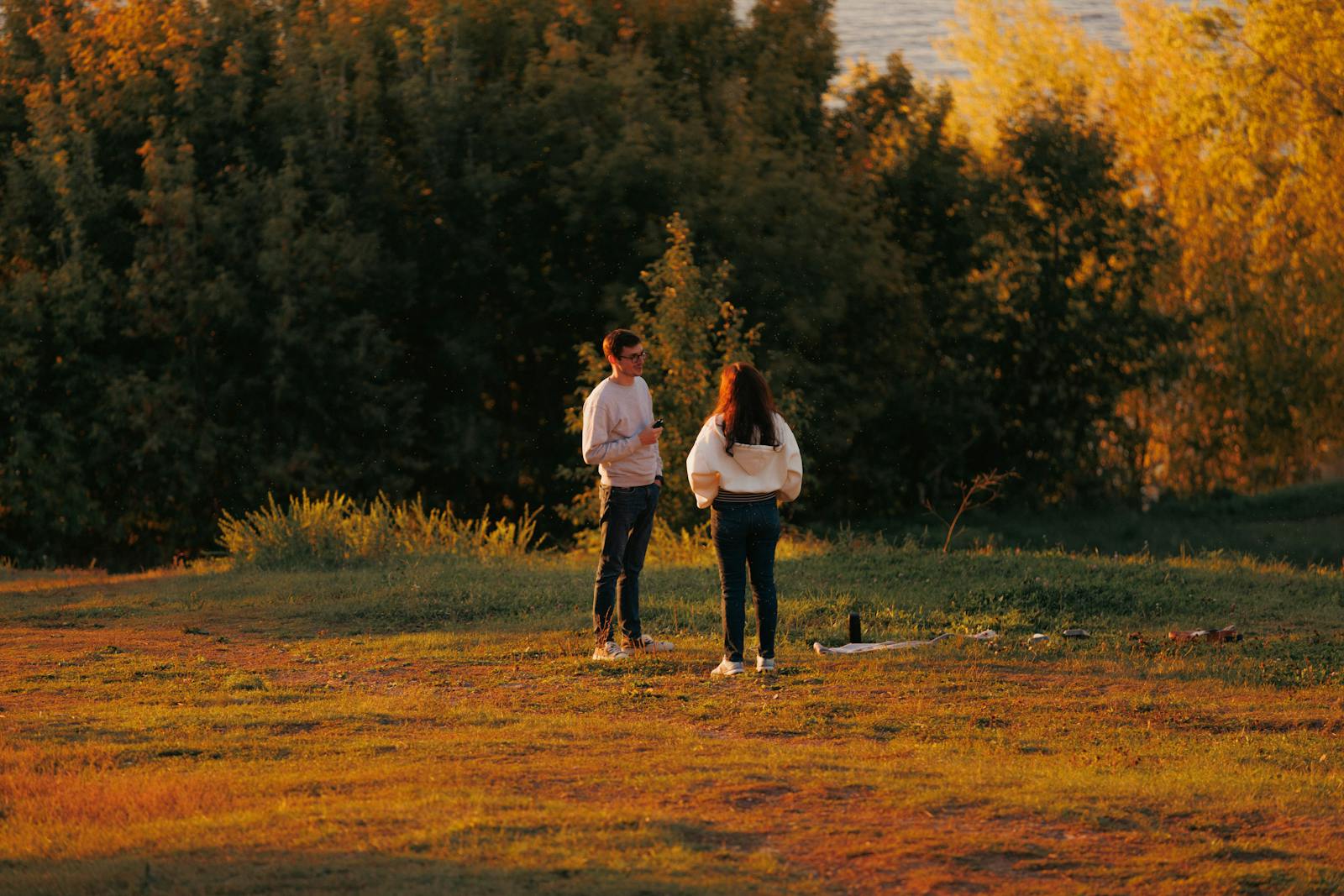 A couple enjoys a peaceful moment in nature at sunset, amidst autumn foliage and warm light.