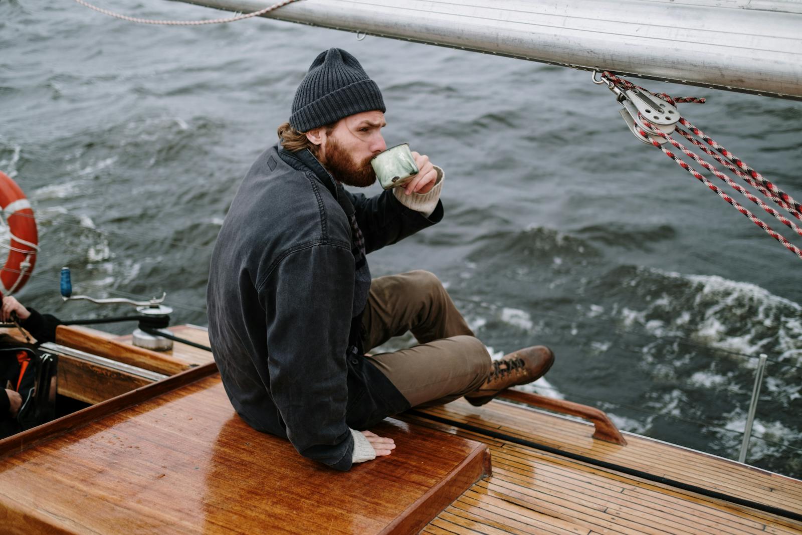 A relaxed man enjoys a hot drink on a sailing boat in open waters.