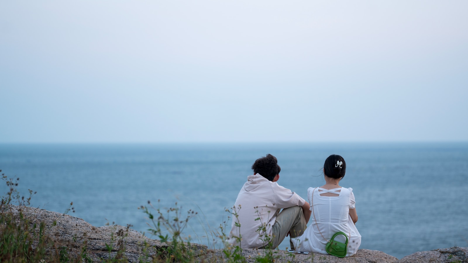 two people sitting on a rock looking out at the ocean